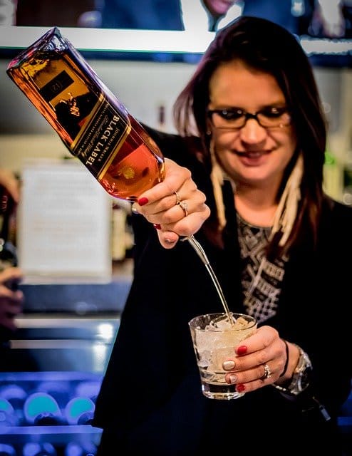 Female bartender pouring Johnnie Walker Black Label into glass with ice.