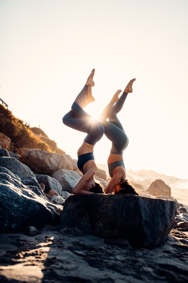 two women do a yoga pose during sunset